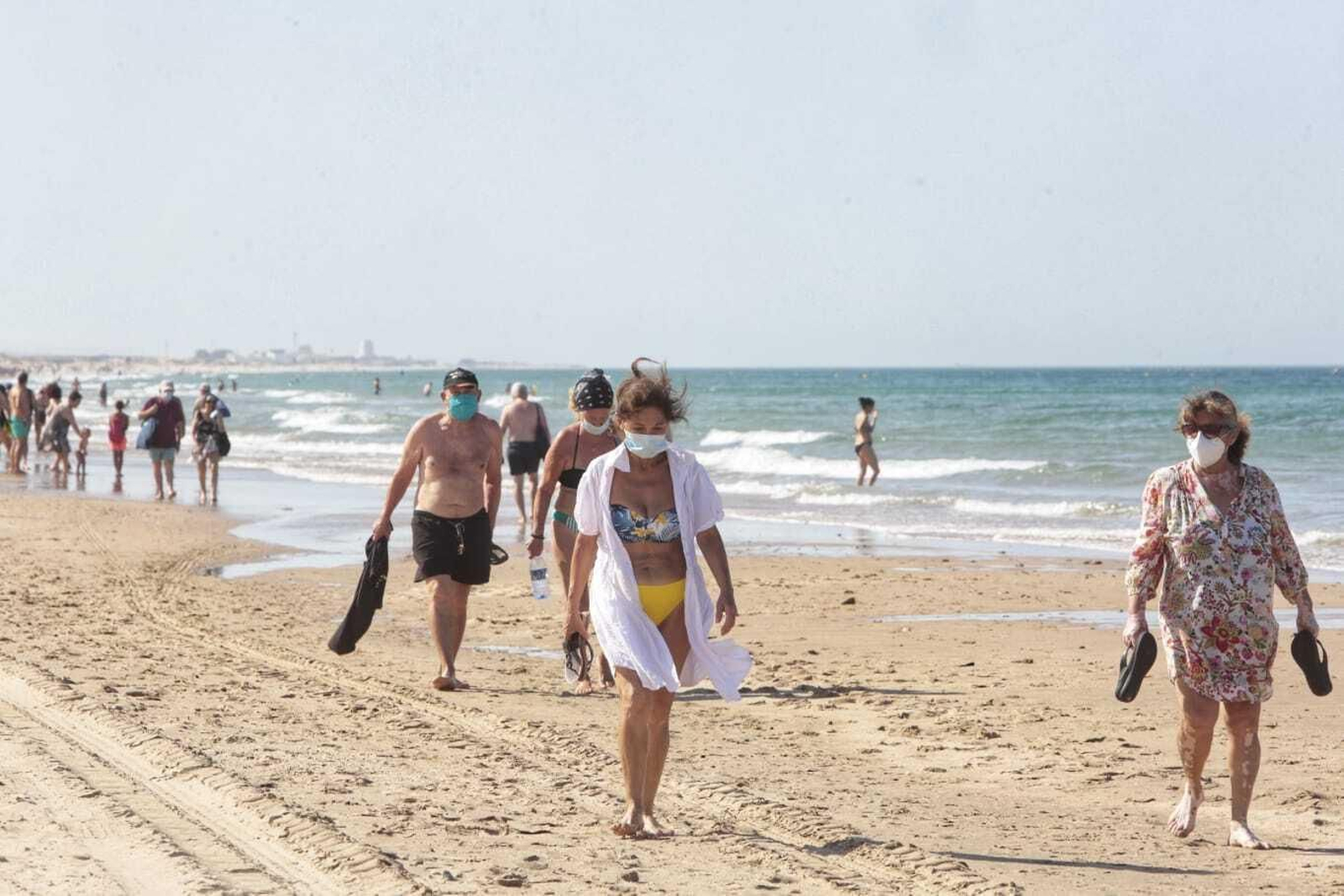 Paseantes con mascarillas en la playa Victoria.