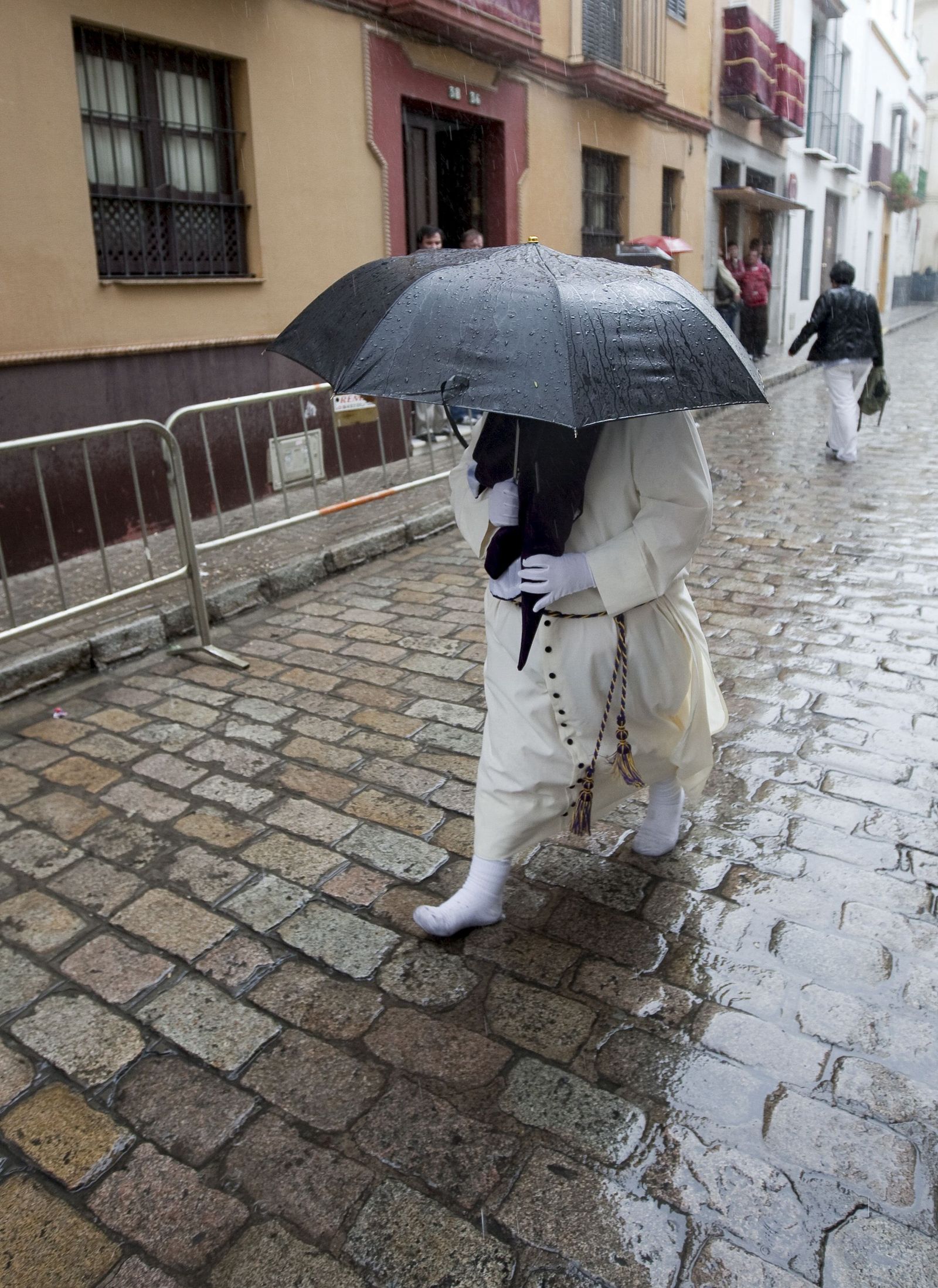 Un nazareno se protege de la lluvia.