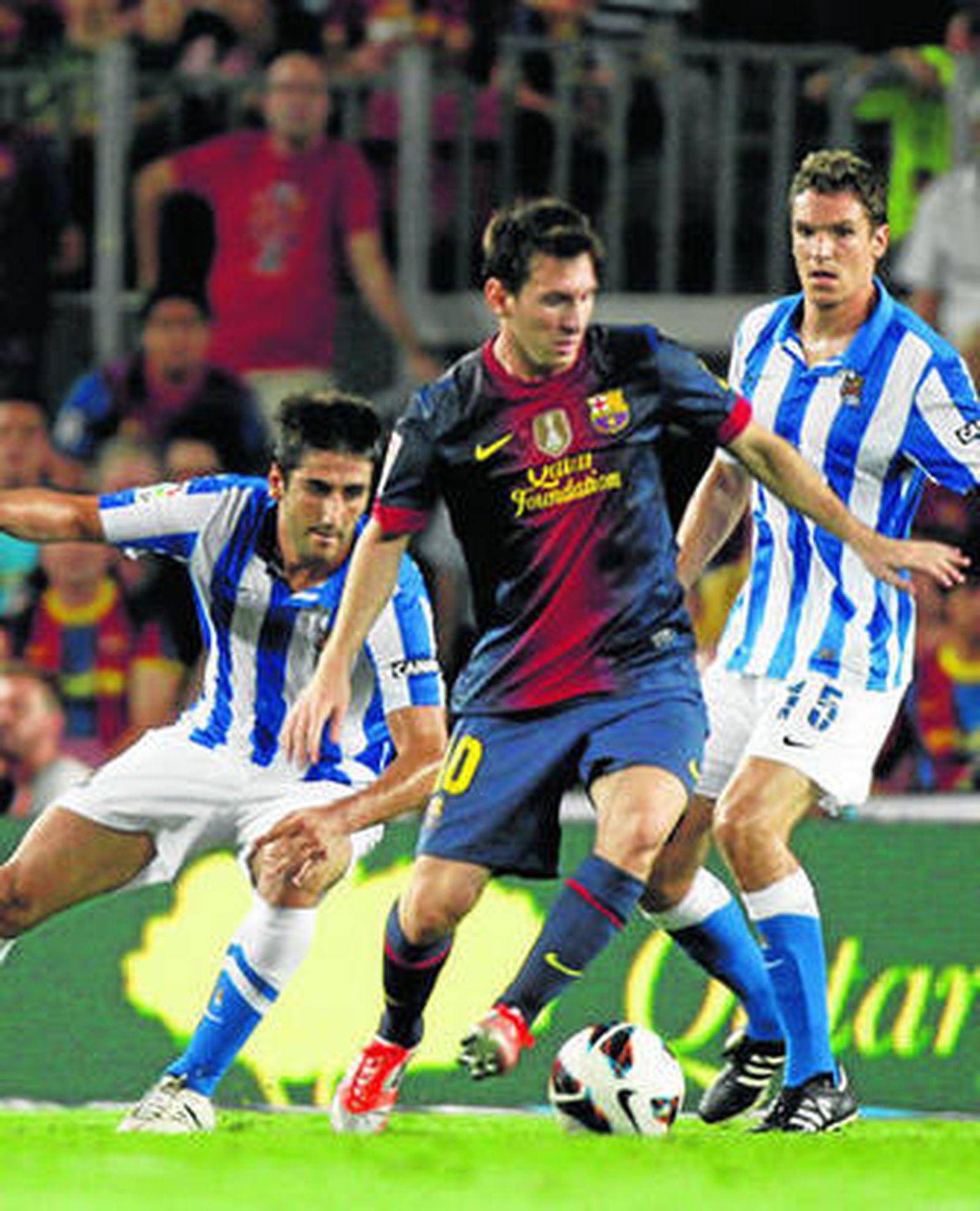 Messi, dándose la vuelta con el balón pegado al pie ante dos jugadores de la Real.