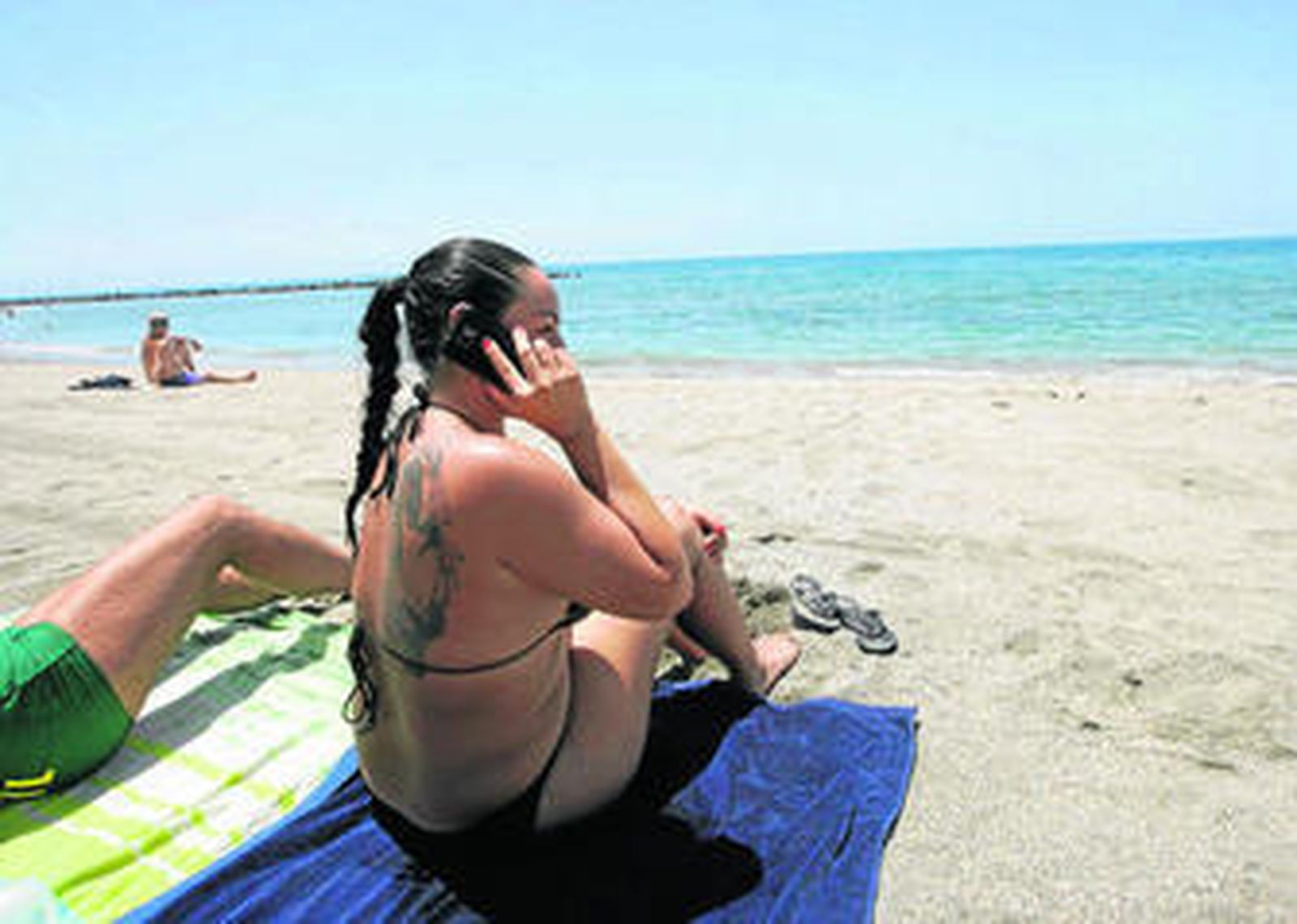 Una joven habla por su móvil mientras toma el sol en la playa.