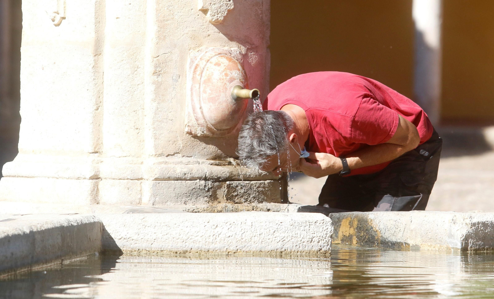 Un hombre se refresca en la fuente del Patio de los Naranjos.