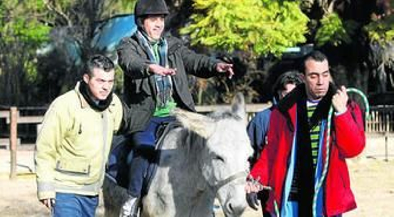 Dos de los residentes de la Casa Familiar San Francisco de Asís ayuda a un tercero mientras realiza su terapia a lomos del burro Lucky.
