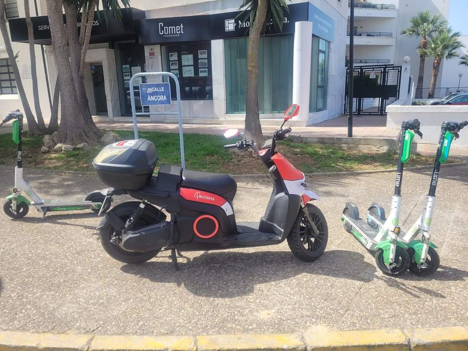 Una moto y varios patinetes en una acera de El Ancla.
