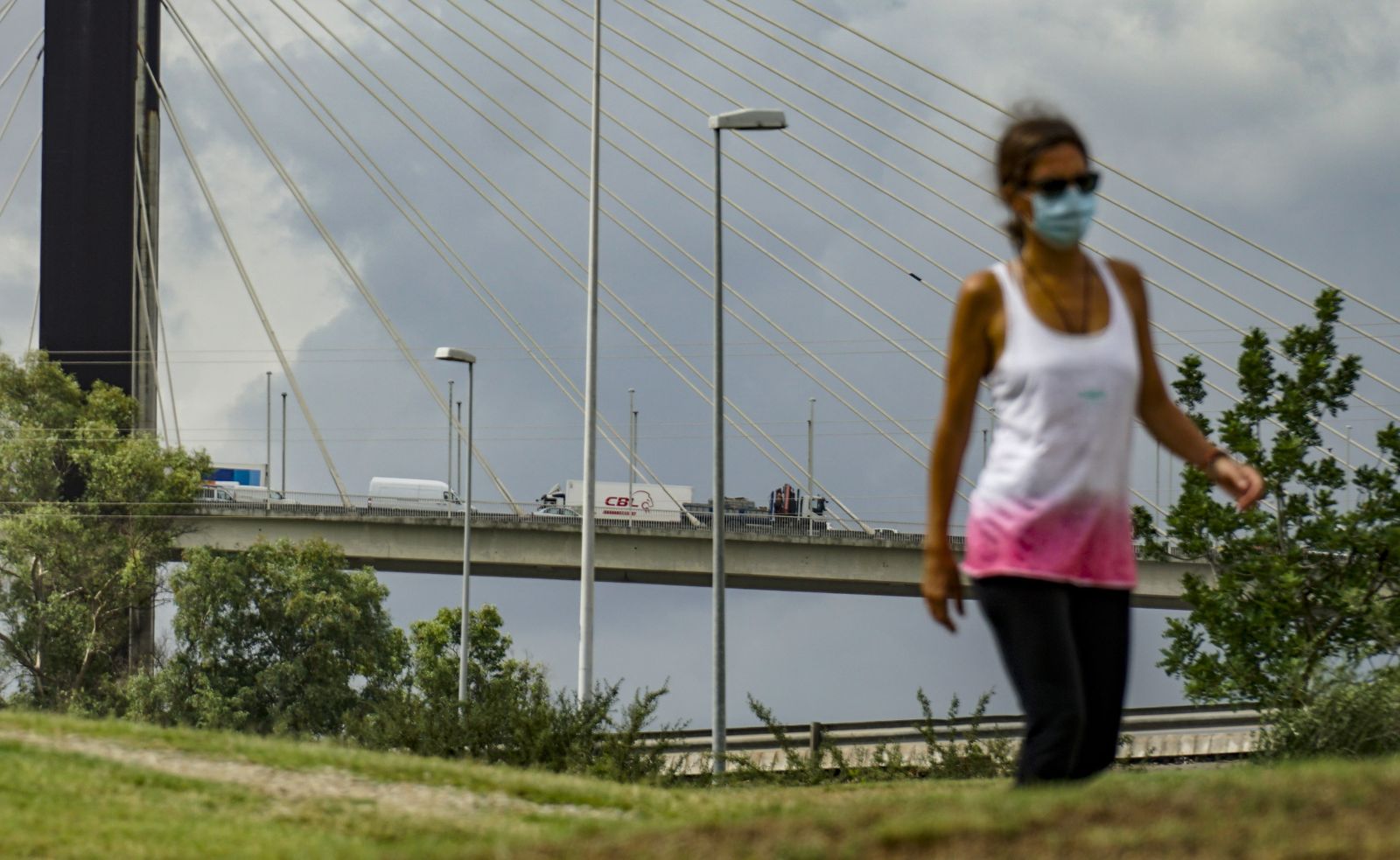 Una deportista camina por el Parque del Guadaíra, situado junto al Puente del Centenario repleto de camiones.