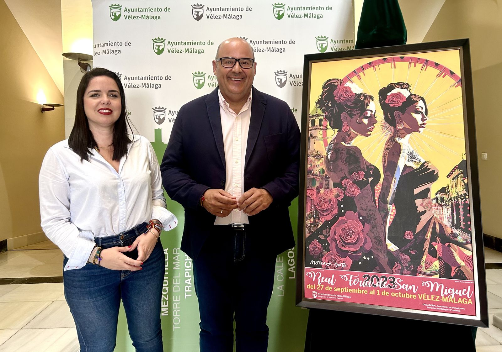 La concejala de Tradiciones Populares, Lourdes Piña y el alcalde Vélez-Málaga, Jesús Lupiáñez, junto al cartel de la Feria de San Miguel
