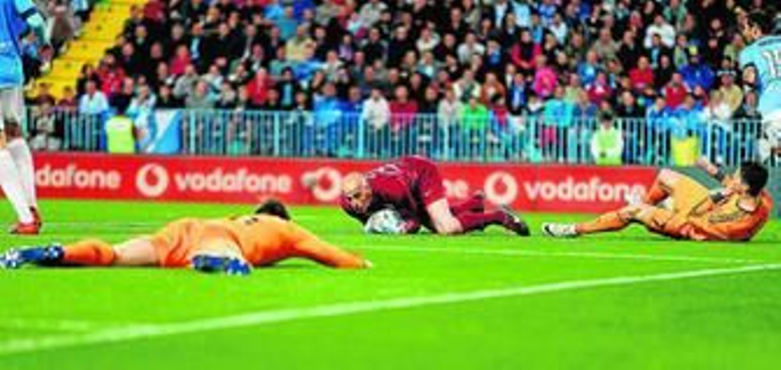Willy Caballero bloca el esférico desde el suelo ante dos jugadores del Real Madrid, en La Rosaleda.