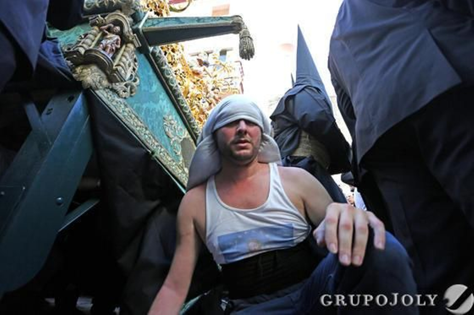 Un costalero del paso del Santísimo Cristo de la Esperanza coge fuerzas sentado en el suelo mientras el misterio está parado en la calle San Juan.

Foto: Pascual