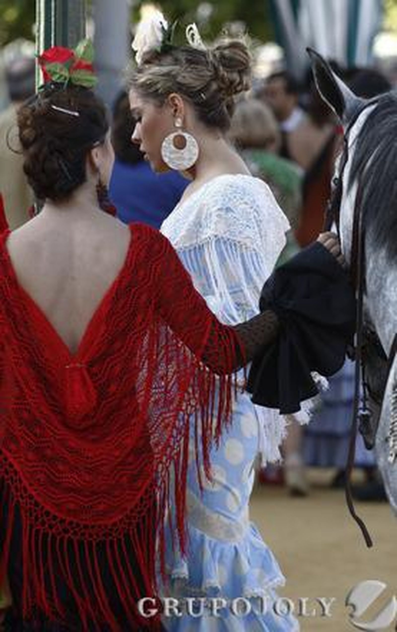 Dos chicas vestidas de flamenca junto a un caballo.

Foto: B.Vargas