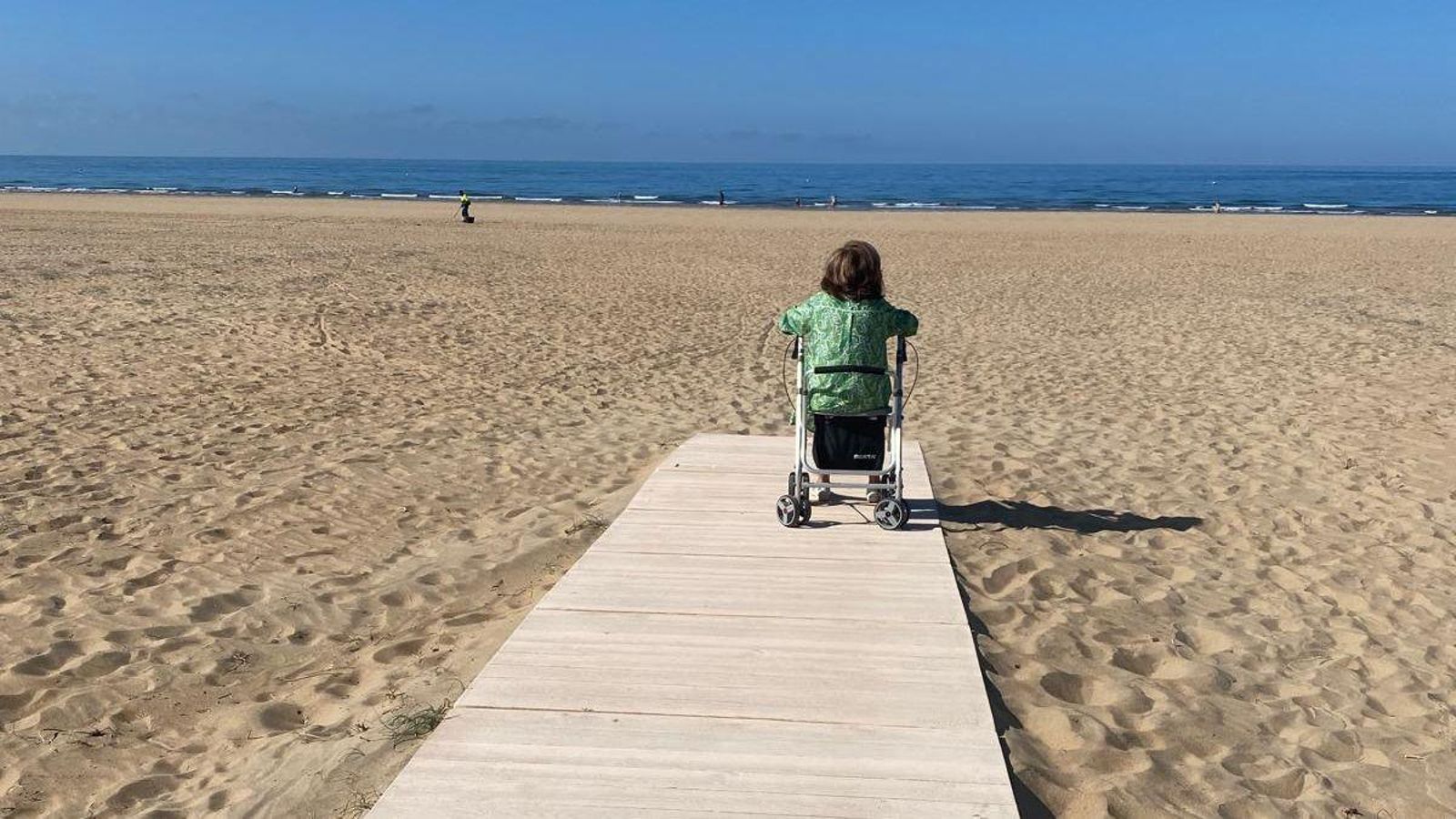 Una mujer observando la playa desde la pasarela y a mucha distancia de la orilla.