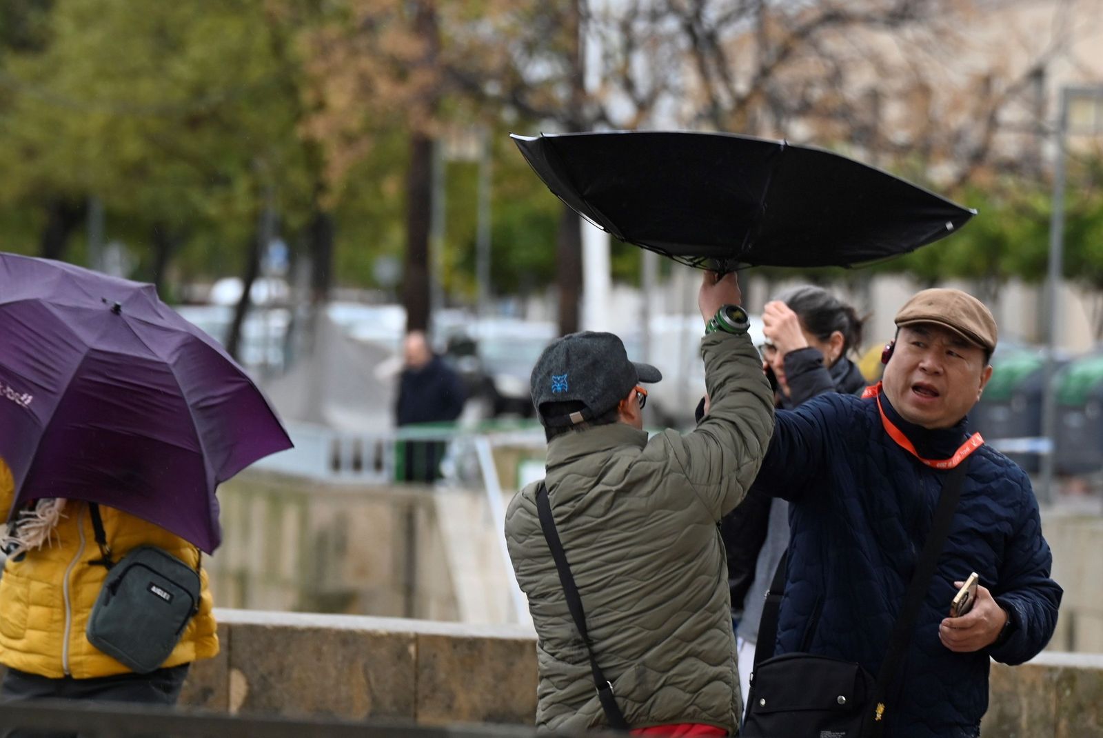 Unos turistas asiáticos desafían a la lluvia y el viento en el entorno del Puente Romano.