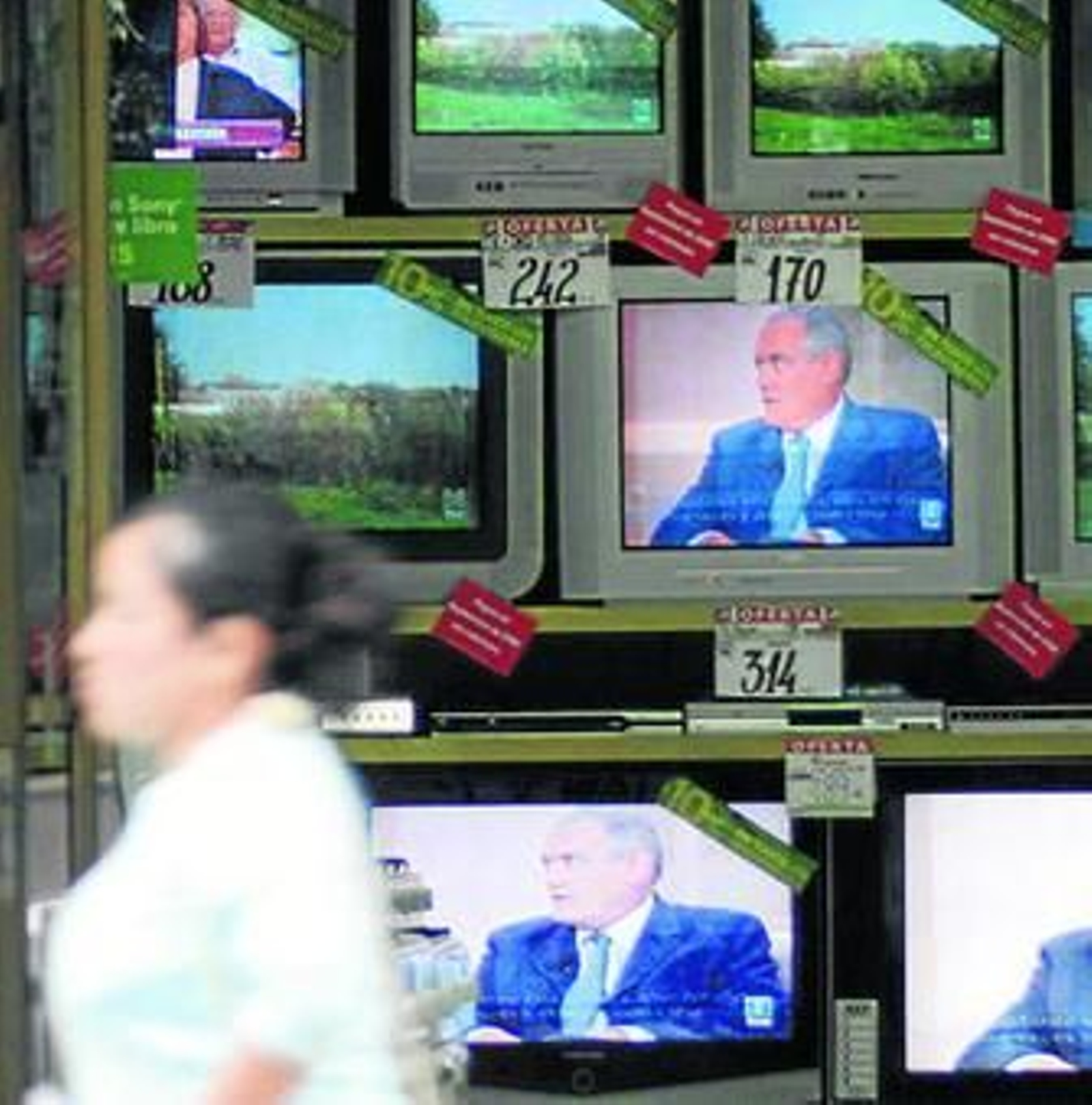 Una mujer pasa ante una tienda de televisores.