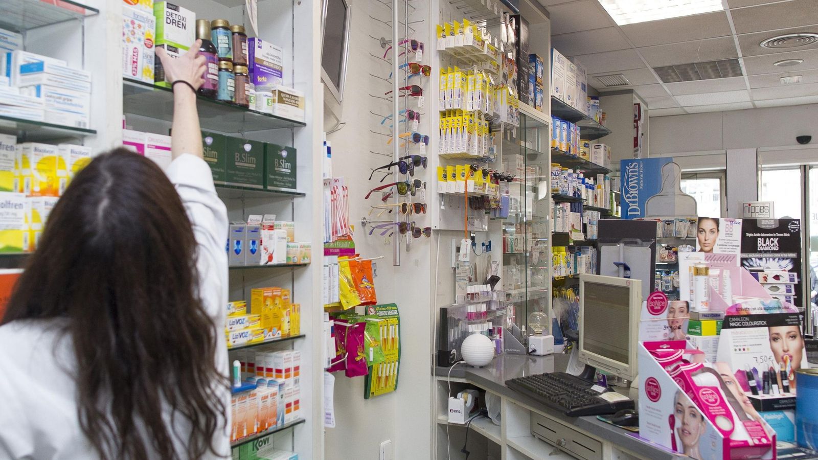Una farmacéutica toma un medicamento de una repisa.