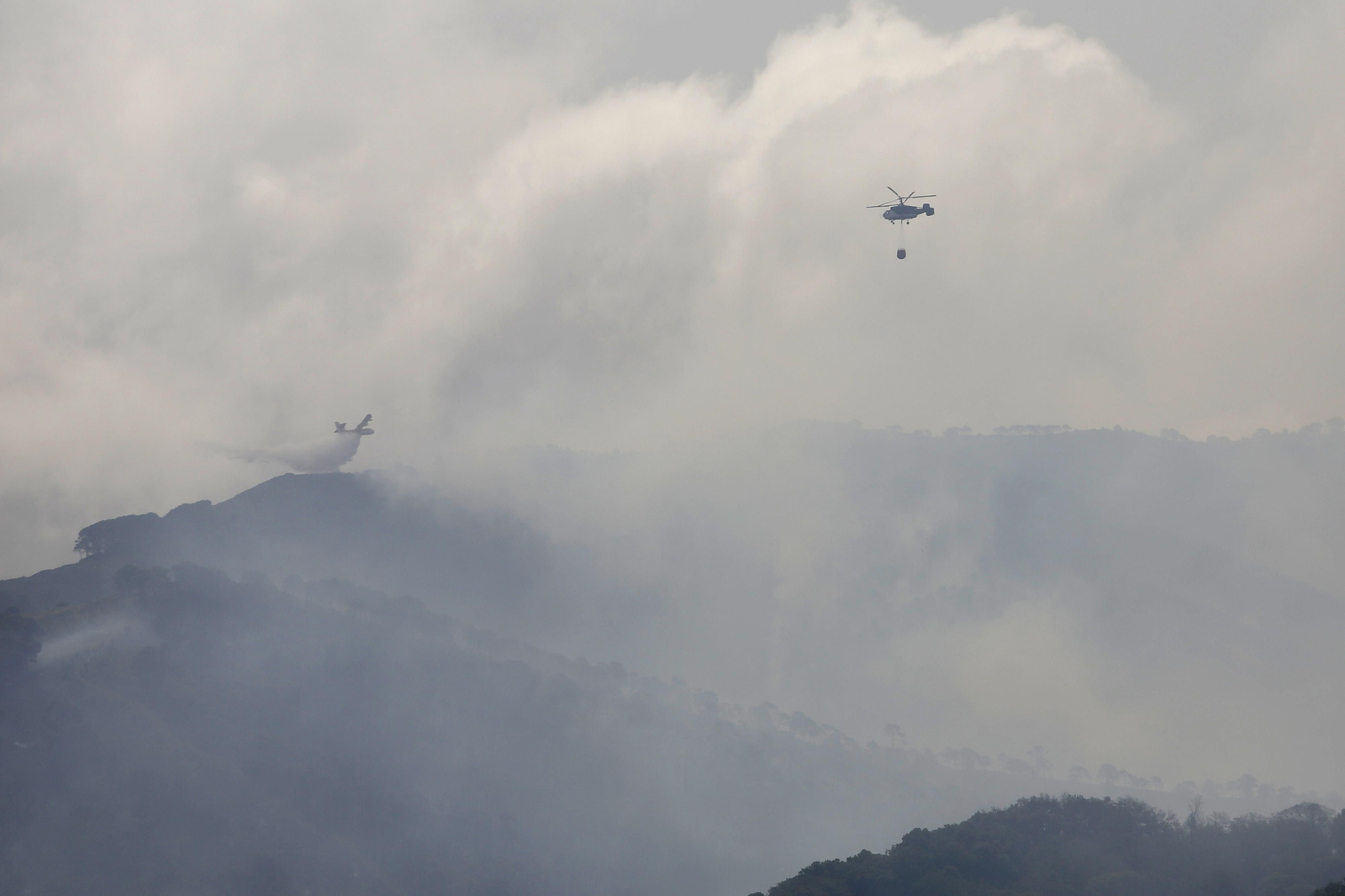 Un hidroavión y un helicóptero Kamov tratan de frenar las llamas en una colina. Un hidroavión y un helicóptero Kamov tratan de frenar las llamas en una colina.