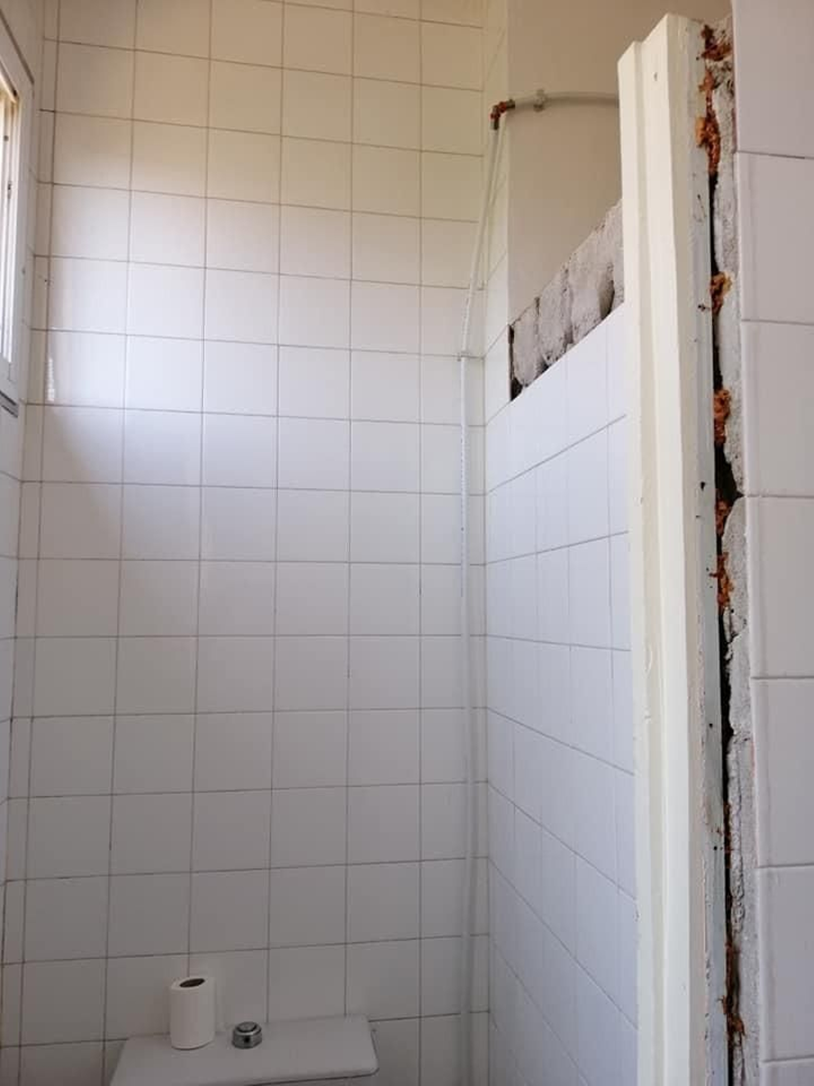 Un baño con azulejos y la puerta arrancada.