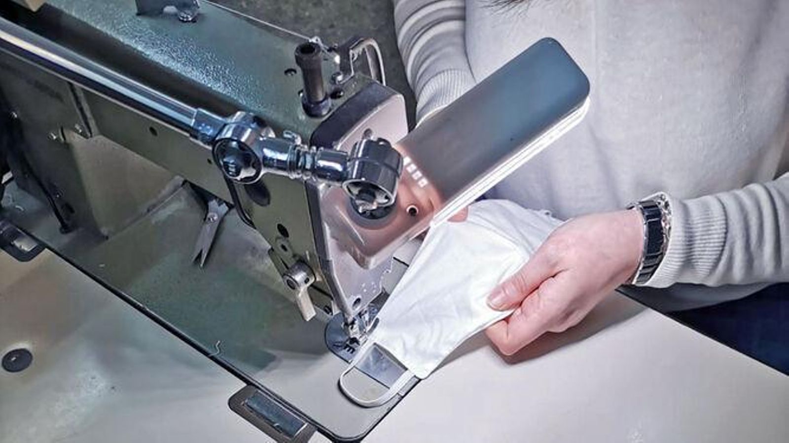 Una costurera cose una mascarilla en una fábrica textil.