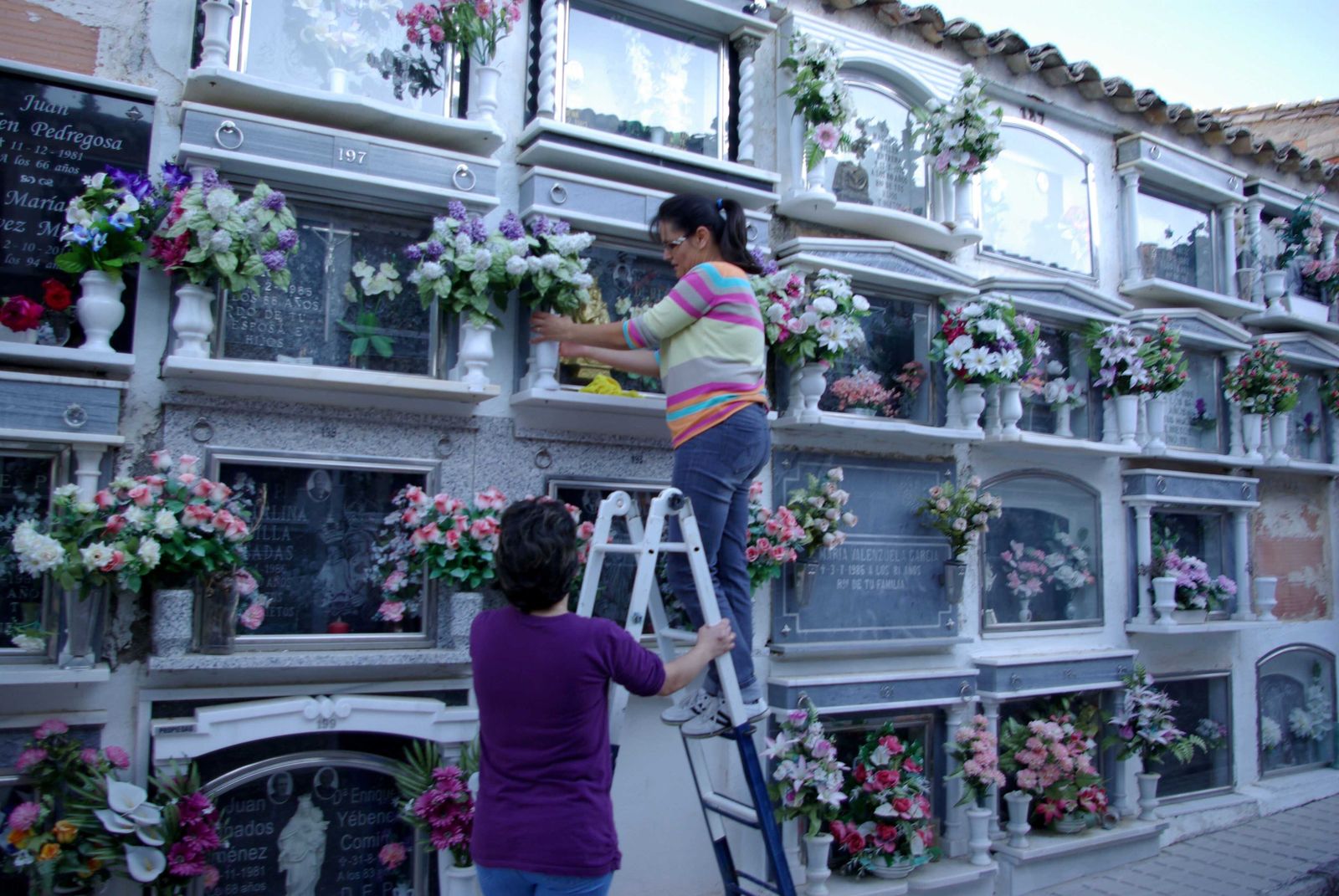 Dos mujeres colocan flores en los nichos del cementerio de Montefrío