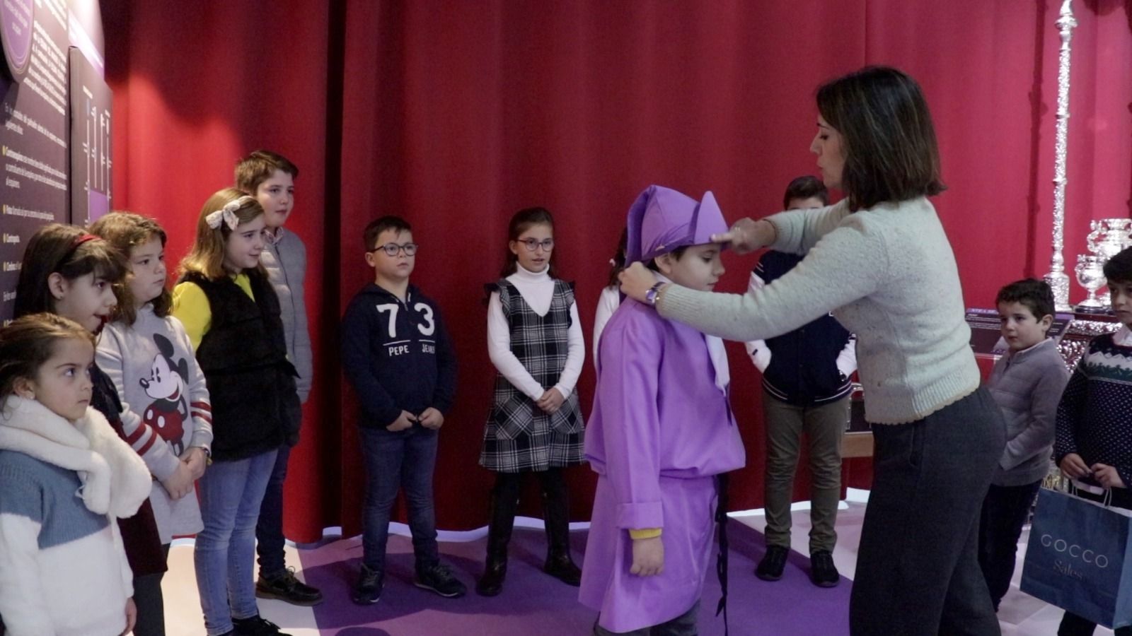 Una mujer comenta ante unos niños los detalles de una vestimenta de Semana Santa.
