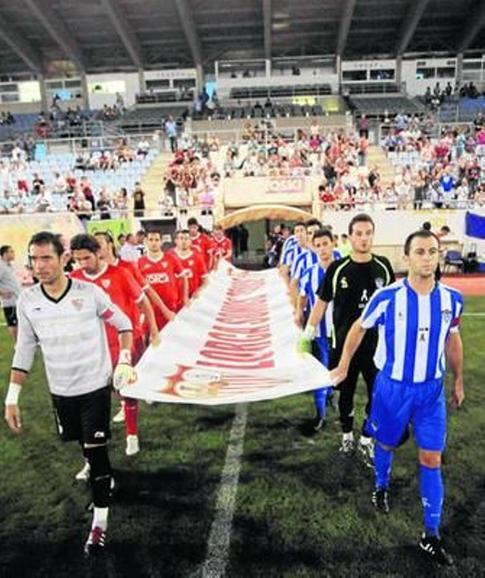 Jugadores del Sevilla (a la izquierda) y el Lorca saltan al campo en un amistoso este verano.