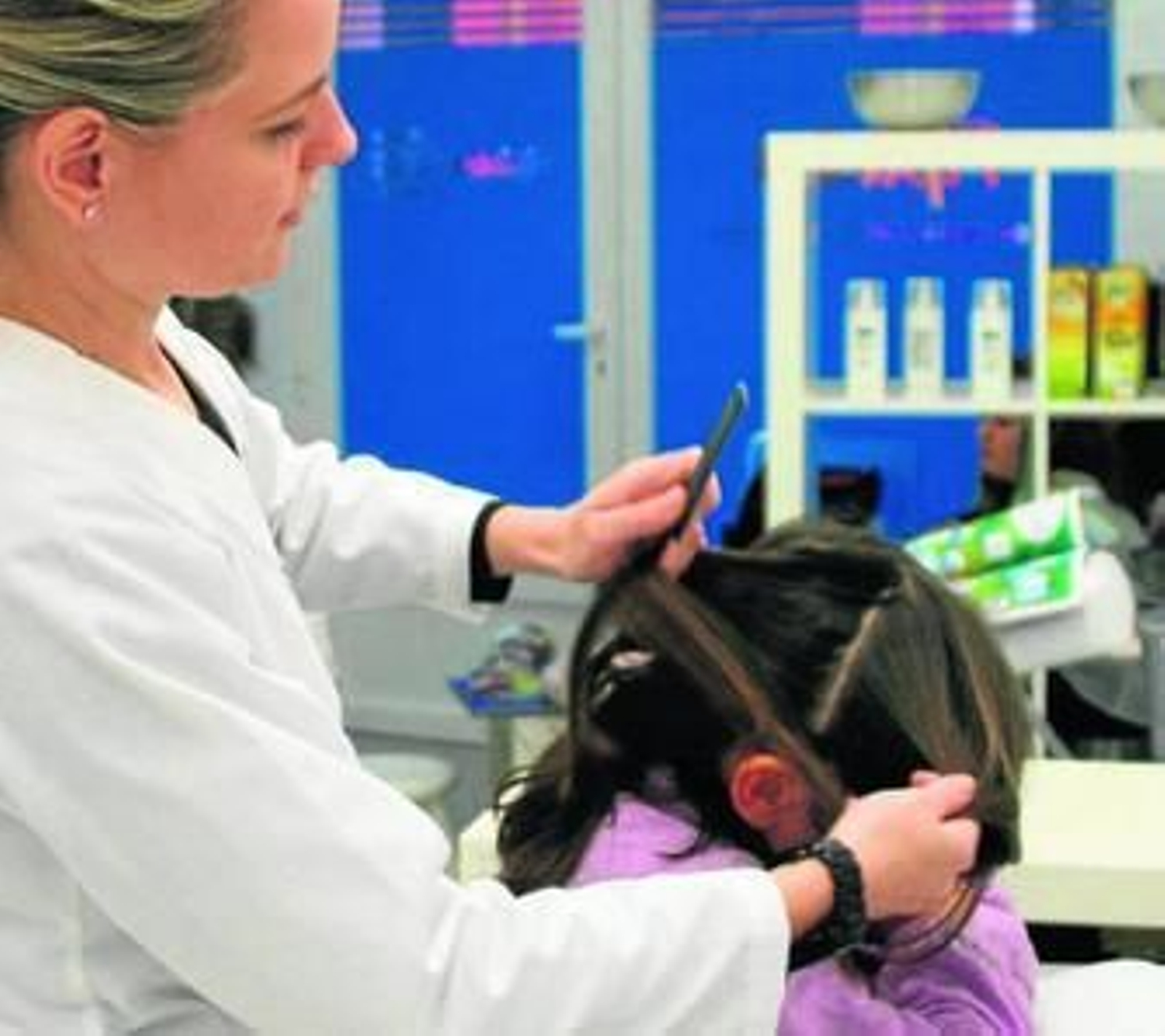 Una empleada de Pipiolos desparasita el cabello de una niña con la lendrera.