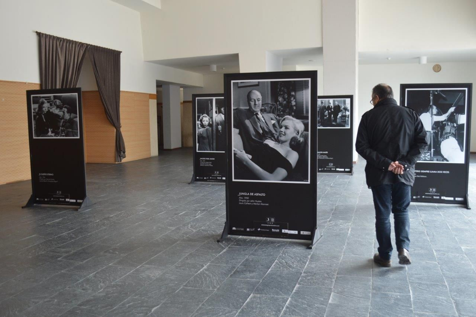 Un visitante pasea entre los cuadros con fotogramas de seis clásicos del cine negro americano. En el centro, Marilyn Monroe, con Louis Calhern, en La jungla de asfalto (John Huston, 1950).