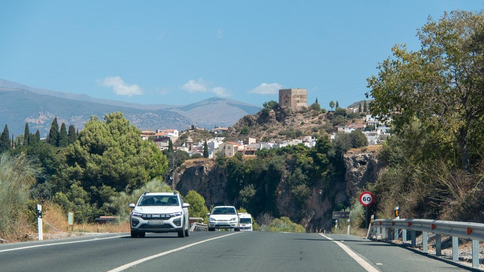Varios coches circulan por la antigua carretera de la costa con Vélez de Benaudalla al fondo
