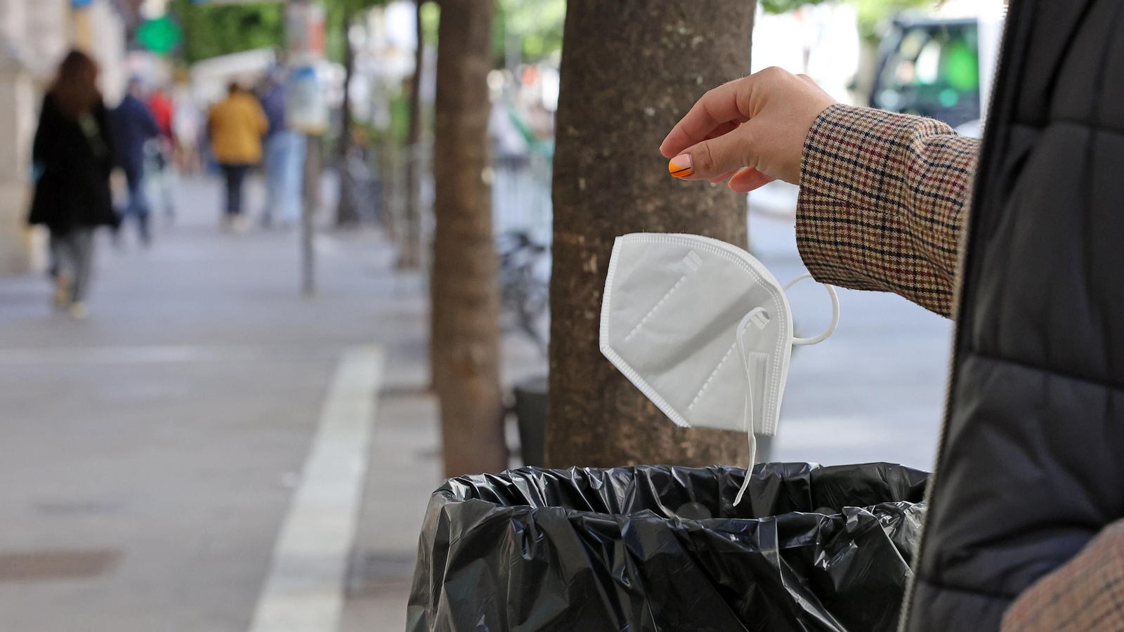 Un ciudadano tira una mascarilla rota a una papelera.