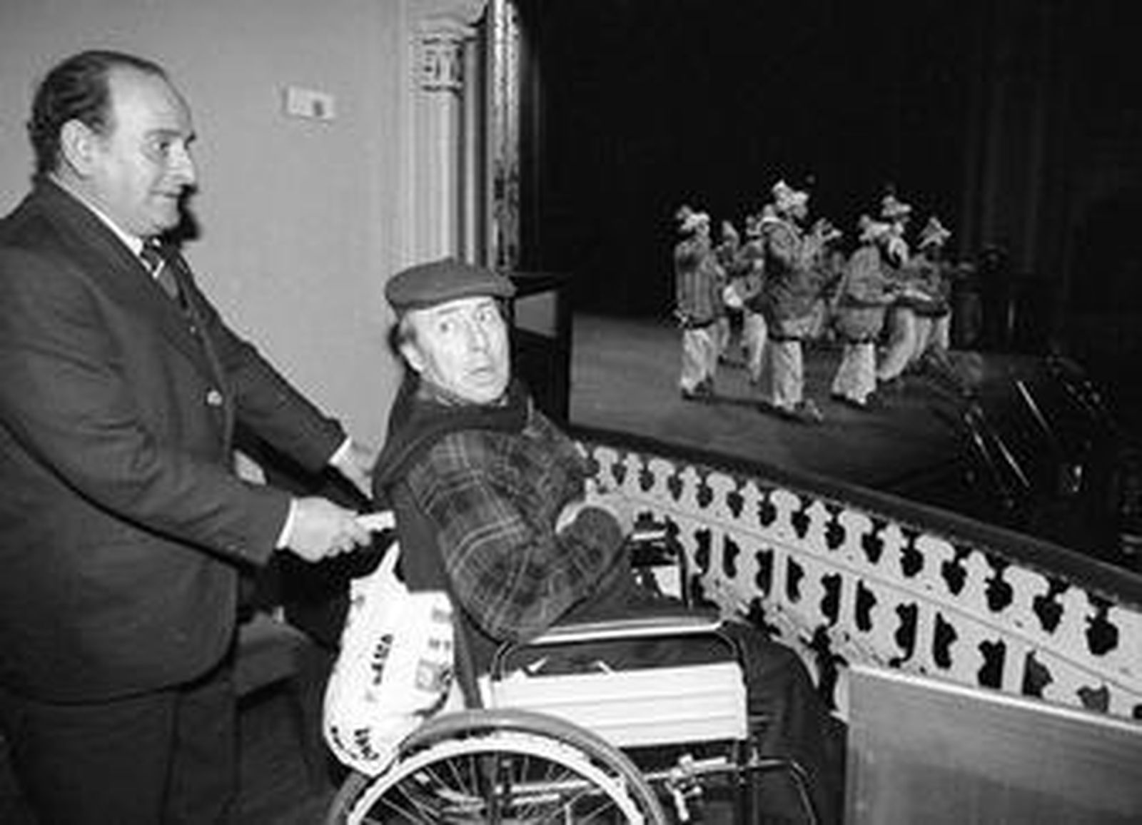 Manuel de Palacio con El Quini, en silla de ruedas, mientras en el escenario actúa 'El ladrón de Bagdá y to los demás de mentida', la primera que cantó en la vuelta al Falla.