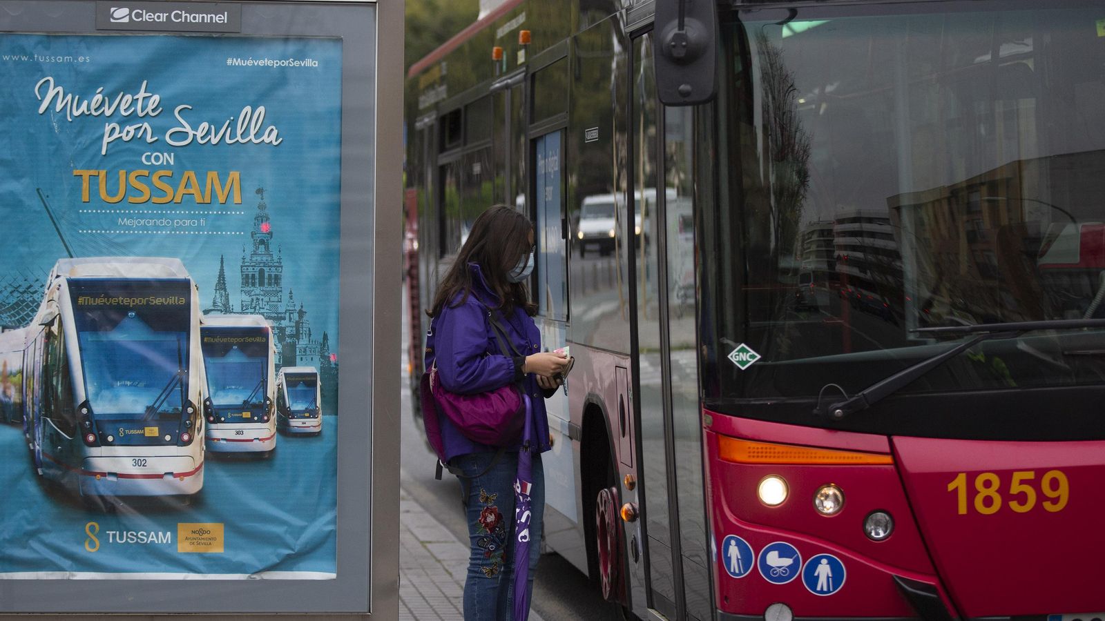 Una mujer, con mascarilla, espera para subir en un autobús de Tussam antes de entrar en vigor la orden de hacerlo por la puerta central.
