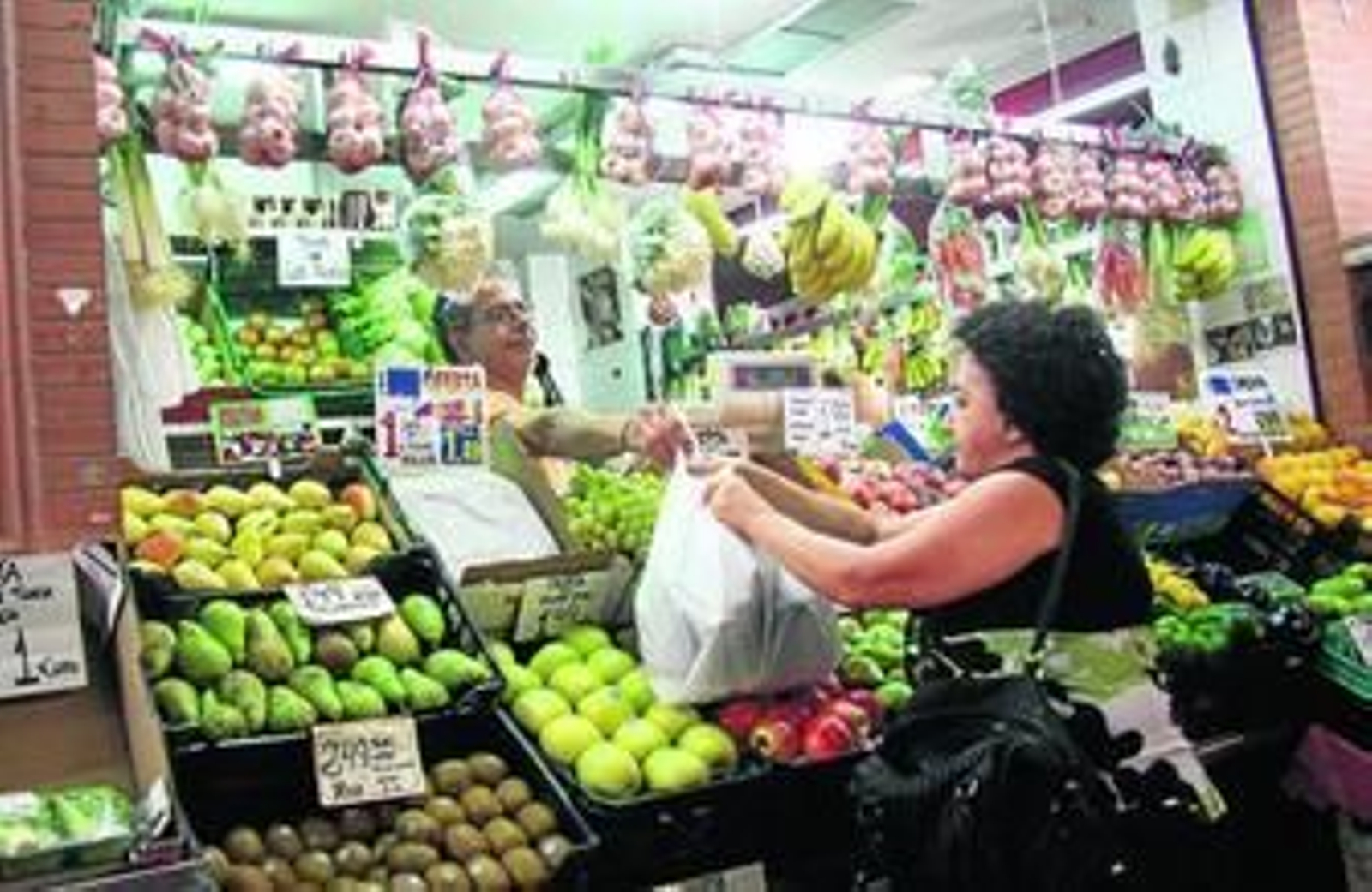 Una mujer compra varios productos en una frutería.