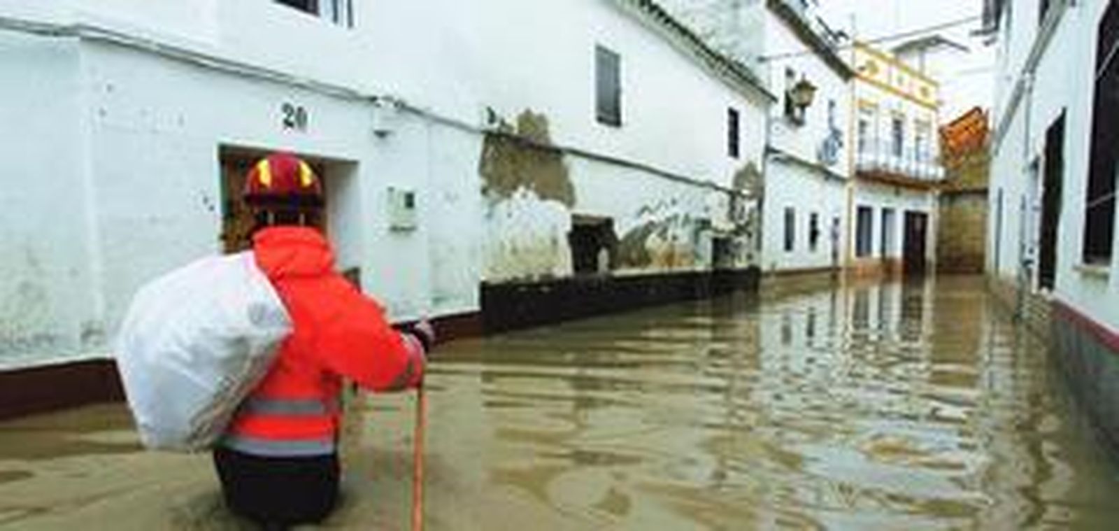 Un voluntario de Protección Civil reparte pan por las casas de una calle anegada de Écija.