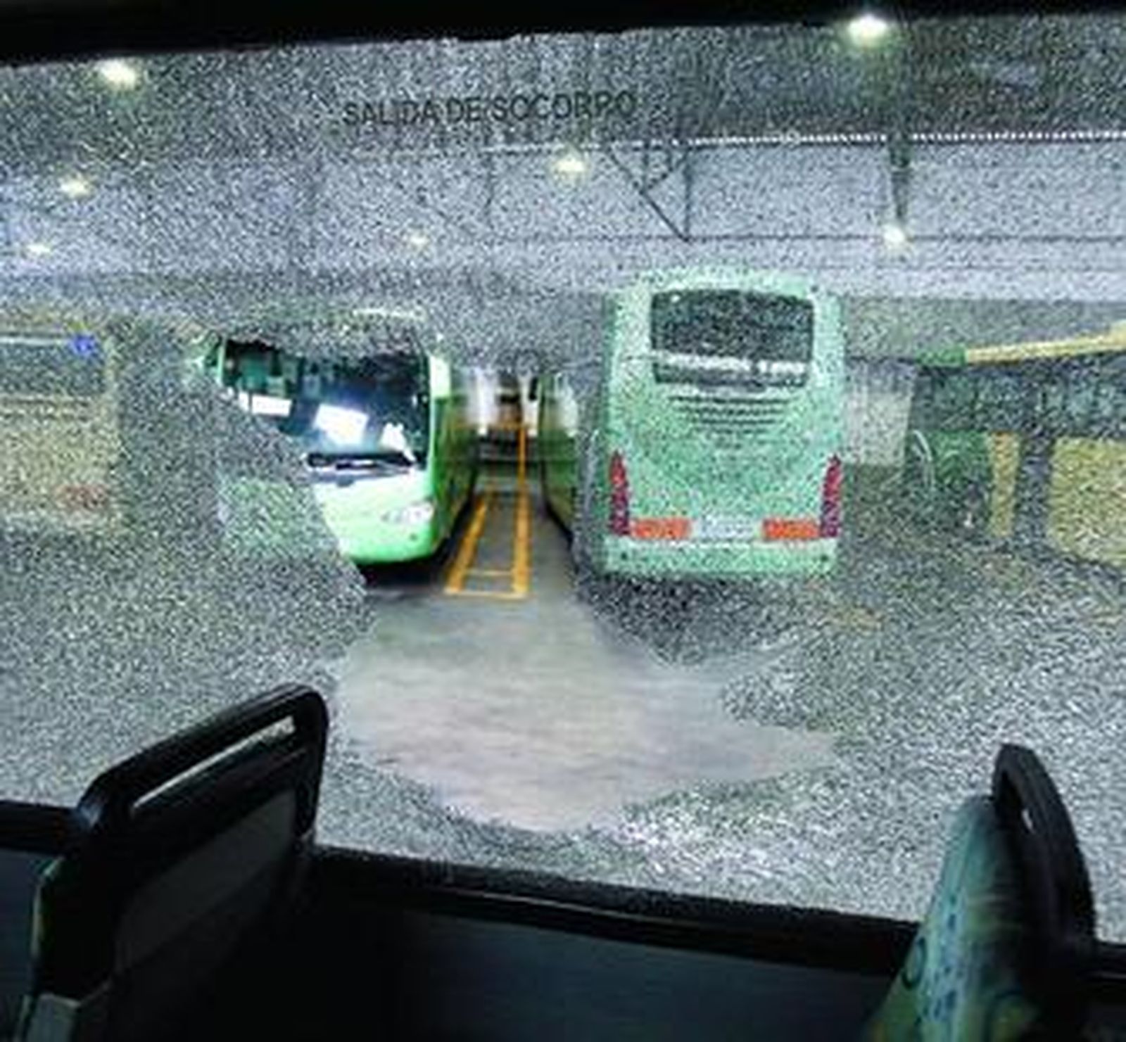 En primer plano, una luna fracturada de un autobús, dentro de las cocheras de Comes, en Zona Franca.