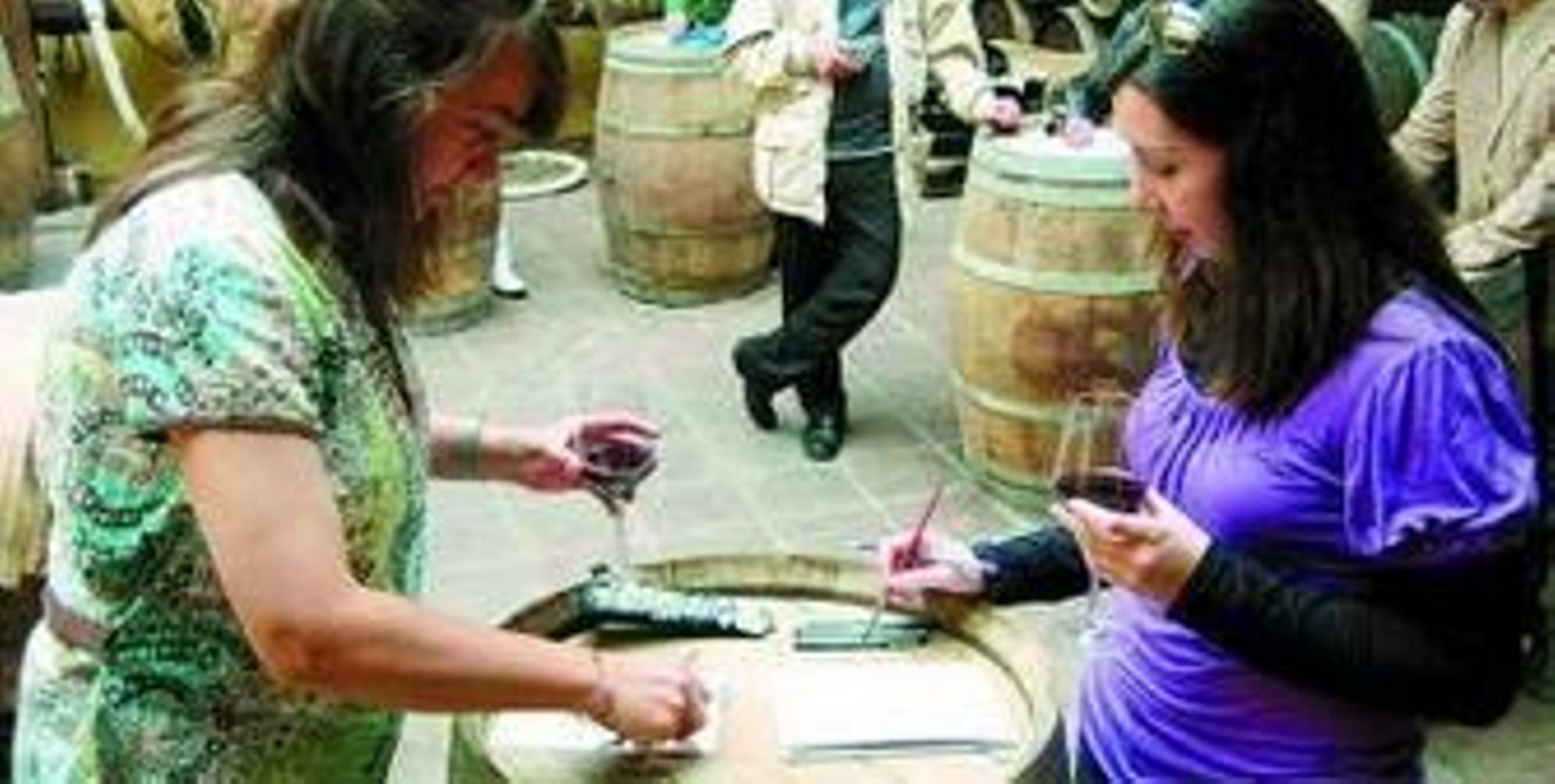 Dos mujeres pintan su obra sobre una barrica de vino.