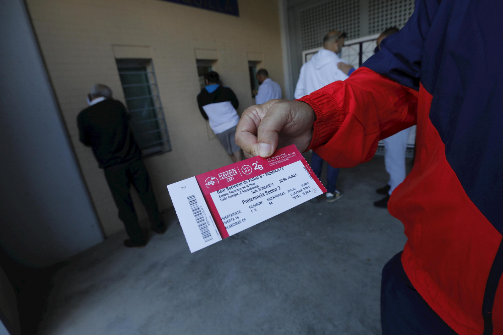 Un aficionado muestra su entrada mientras otros son atendidos en las ventanillas.