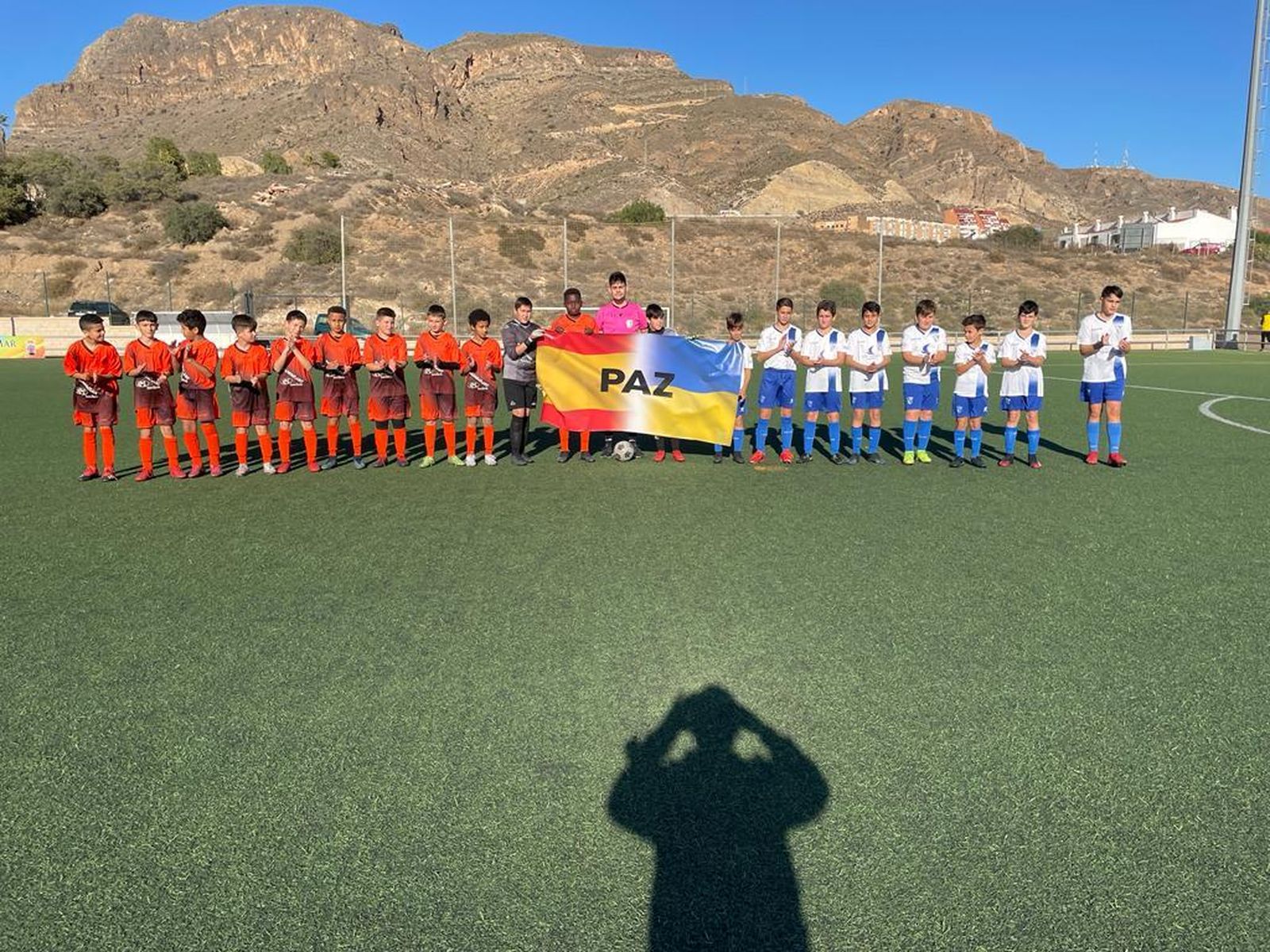 Los alevines de La Mojonera (izquierda) y del Poli Aguadulce (derecha), en el partido del pasado fin de semana con una bandera por la paz.