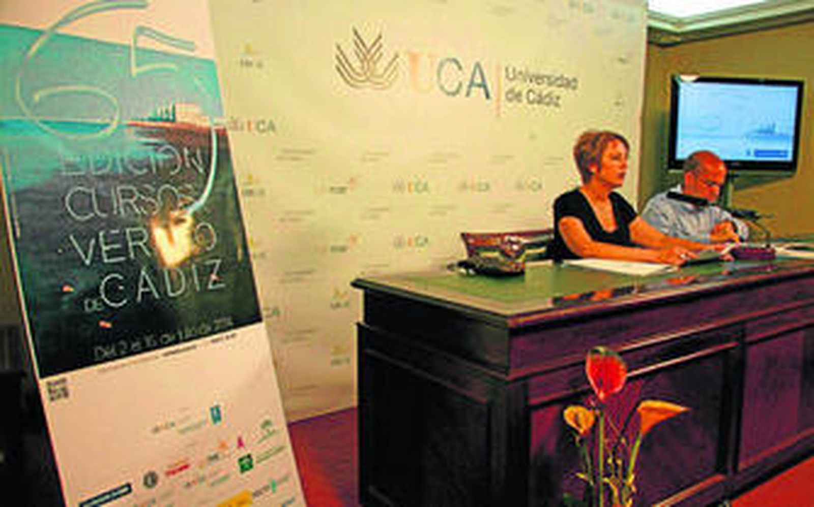 Acto de presentación de los Cursos de Verano, con el cartel realizado por el artista Pepe Baena en primer plano.