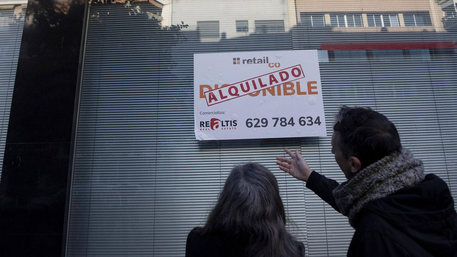 Dos personas observan un cartel de un inmueble ya alquilado.