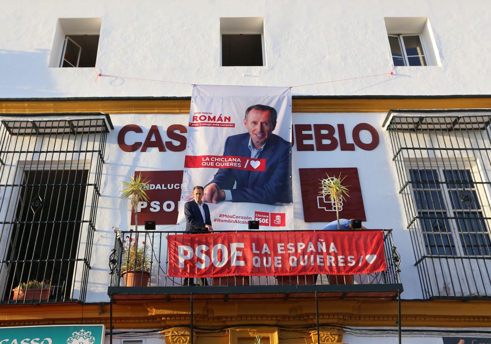 Román junto al enorme cartel con su rostro en la fachada de la sede socialista.