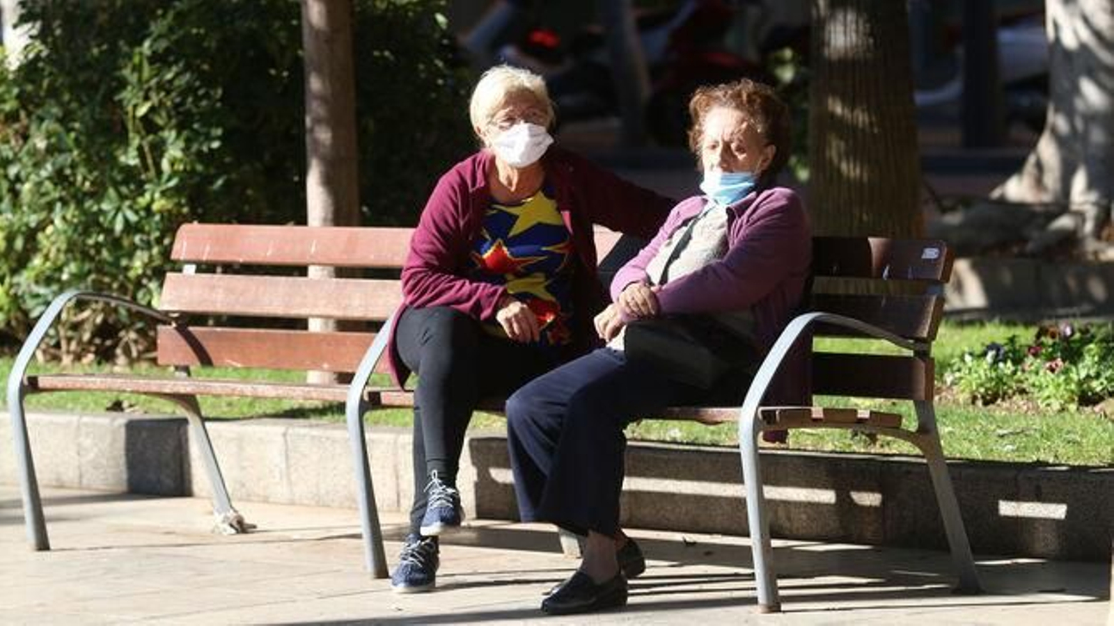 Dos personas mayores dialogan en uno de los bancos de la Rambla.