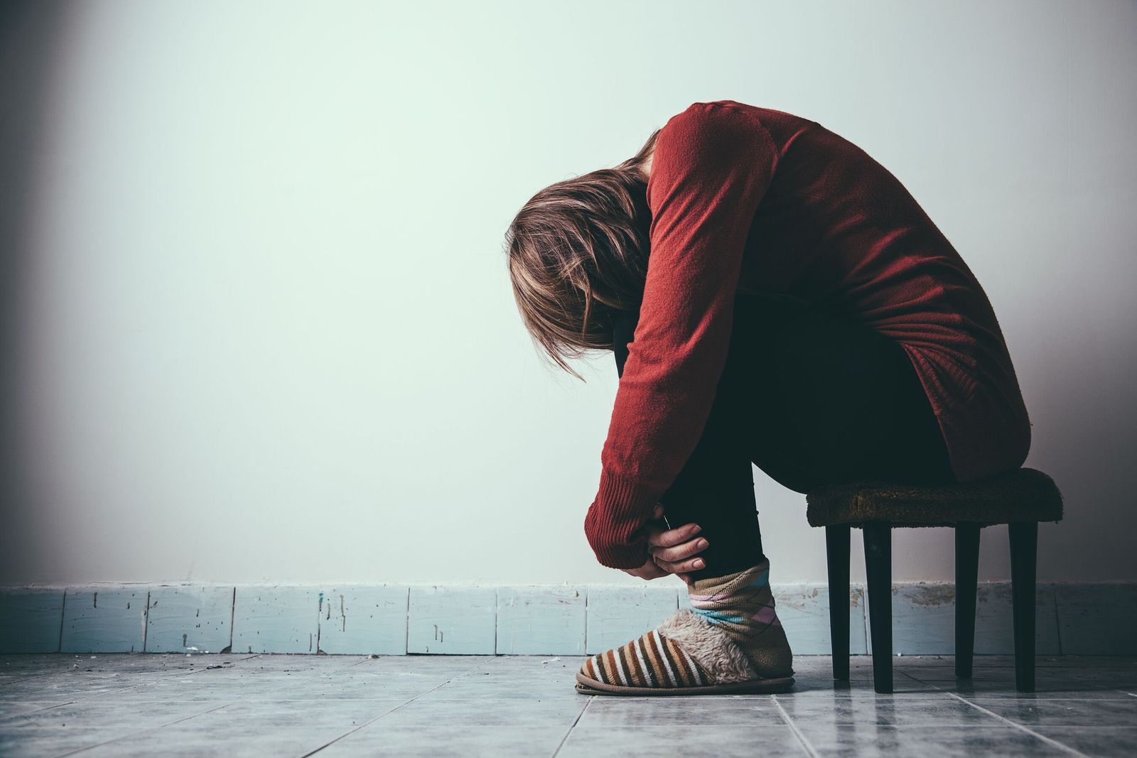 Una mujer se abraza las piernas sentada en un taburete.