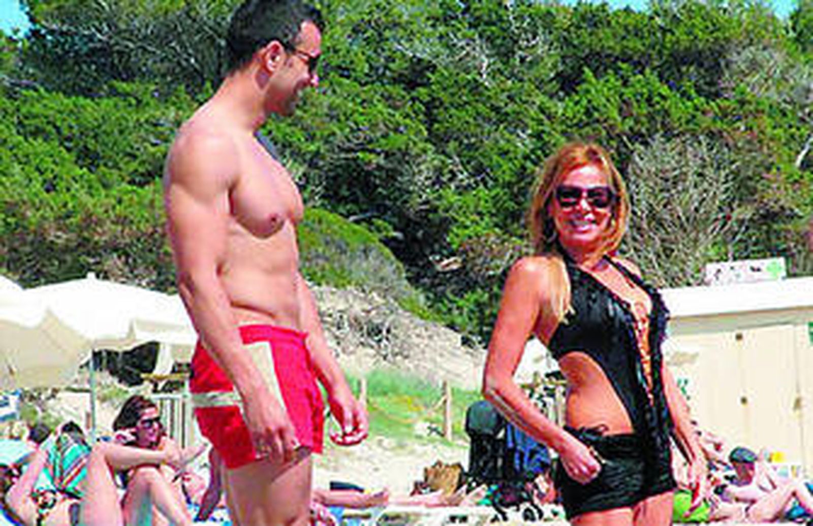 La bióloga, con un trikini, en la playa al lado de su atlético amigo.