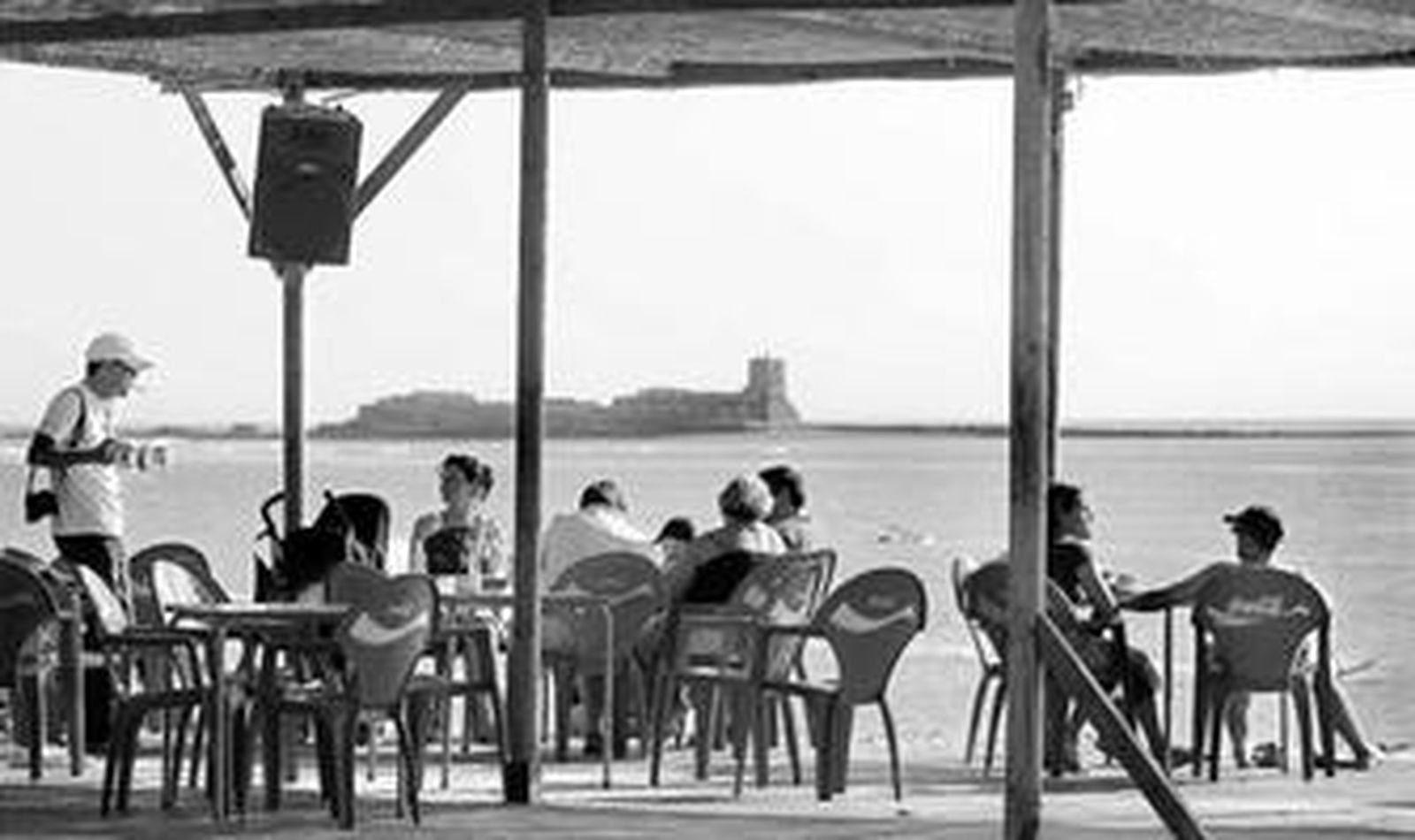 Unos turistas disfrutan de unos refrescos en uno de los chiringuitos que el pasado verano se instalaron frente al Castillo de Sancti Petri.