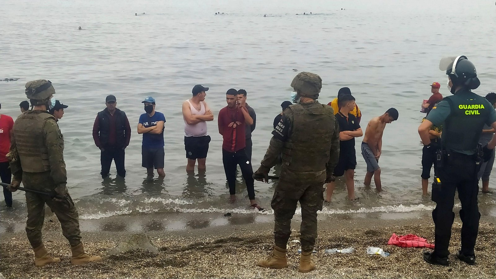 Miembros de la Guardia Civil y el Ejército, con un grupo de migrantes en la playa de Ceuta.