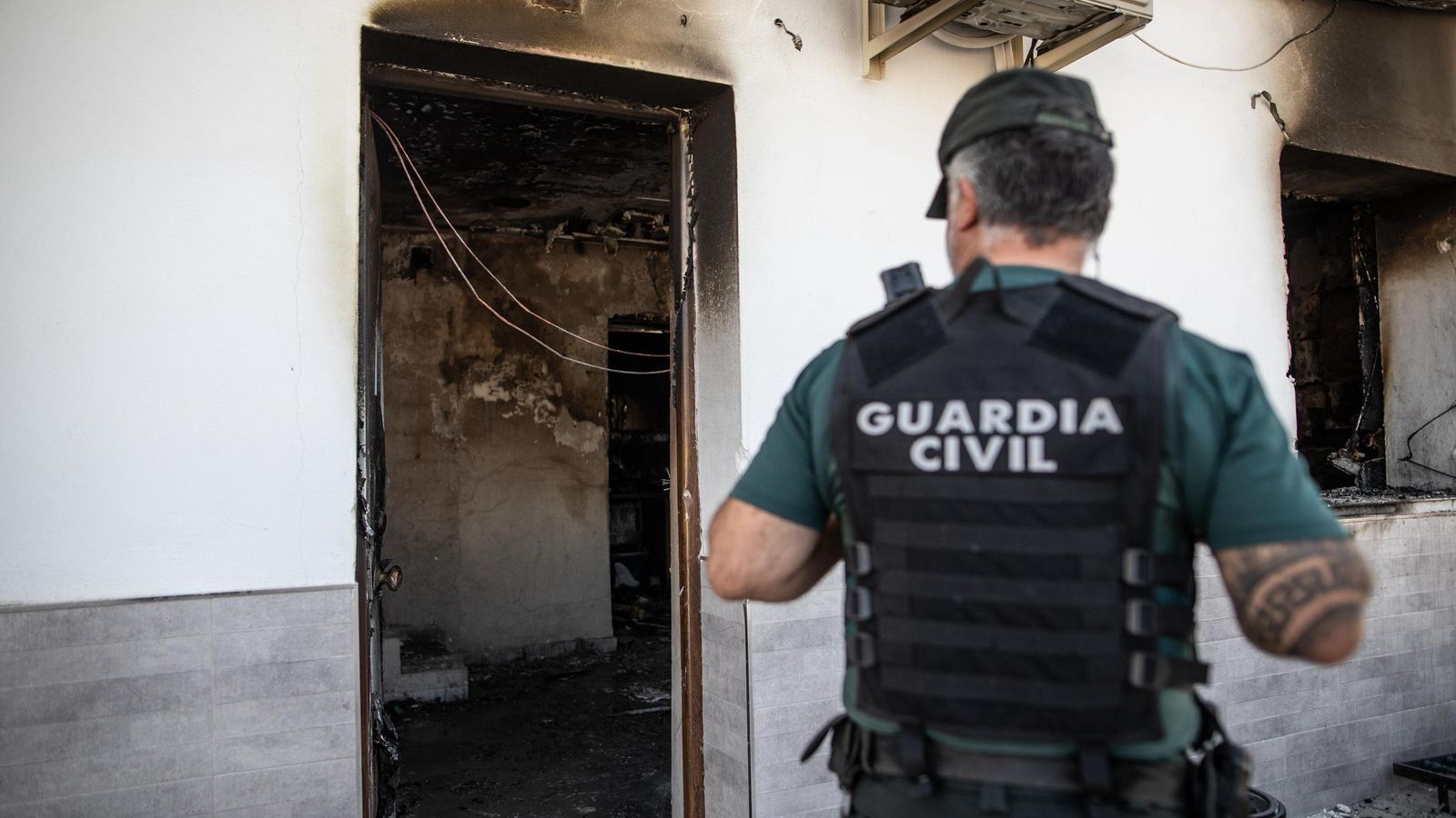 Un agente frente a una de las casas calcinadas en Pinos Puente