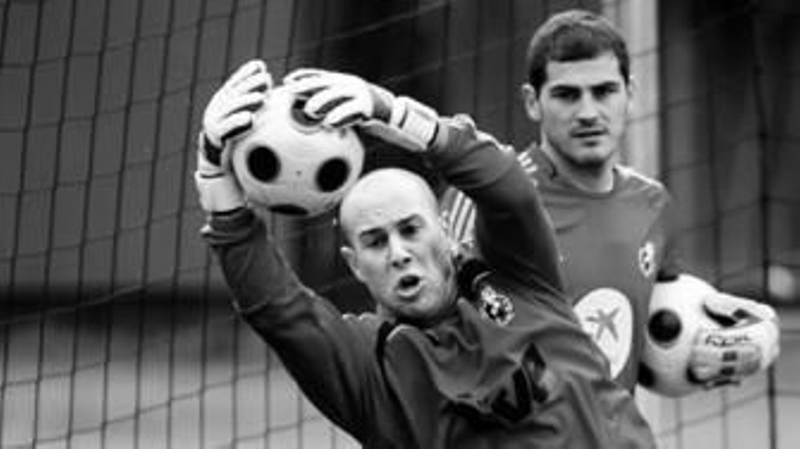 El portero español Reina detiene un balón con las dos manos ante la mirada de Iker Casillas.