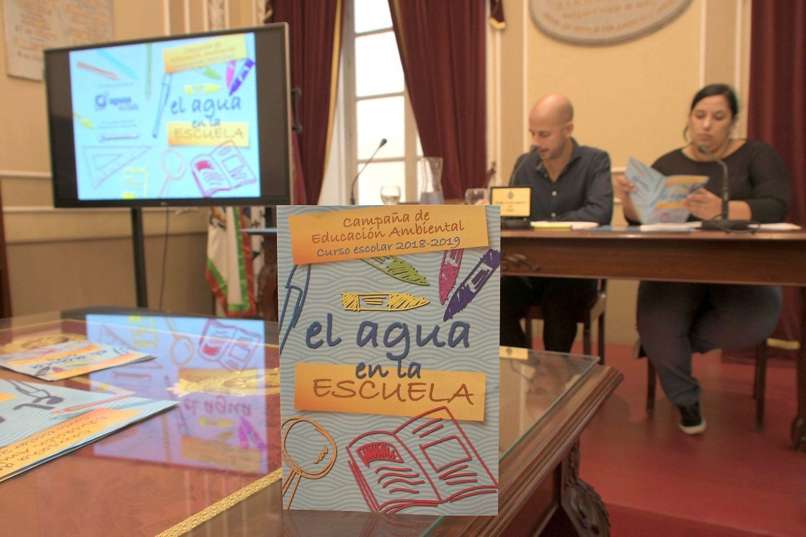 El cartel de la campaña con Álvaro de la Fuente y Ana Fernández al fondo