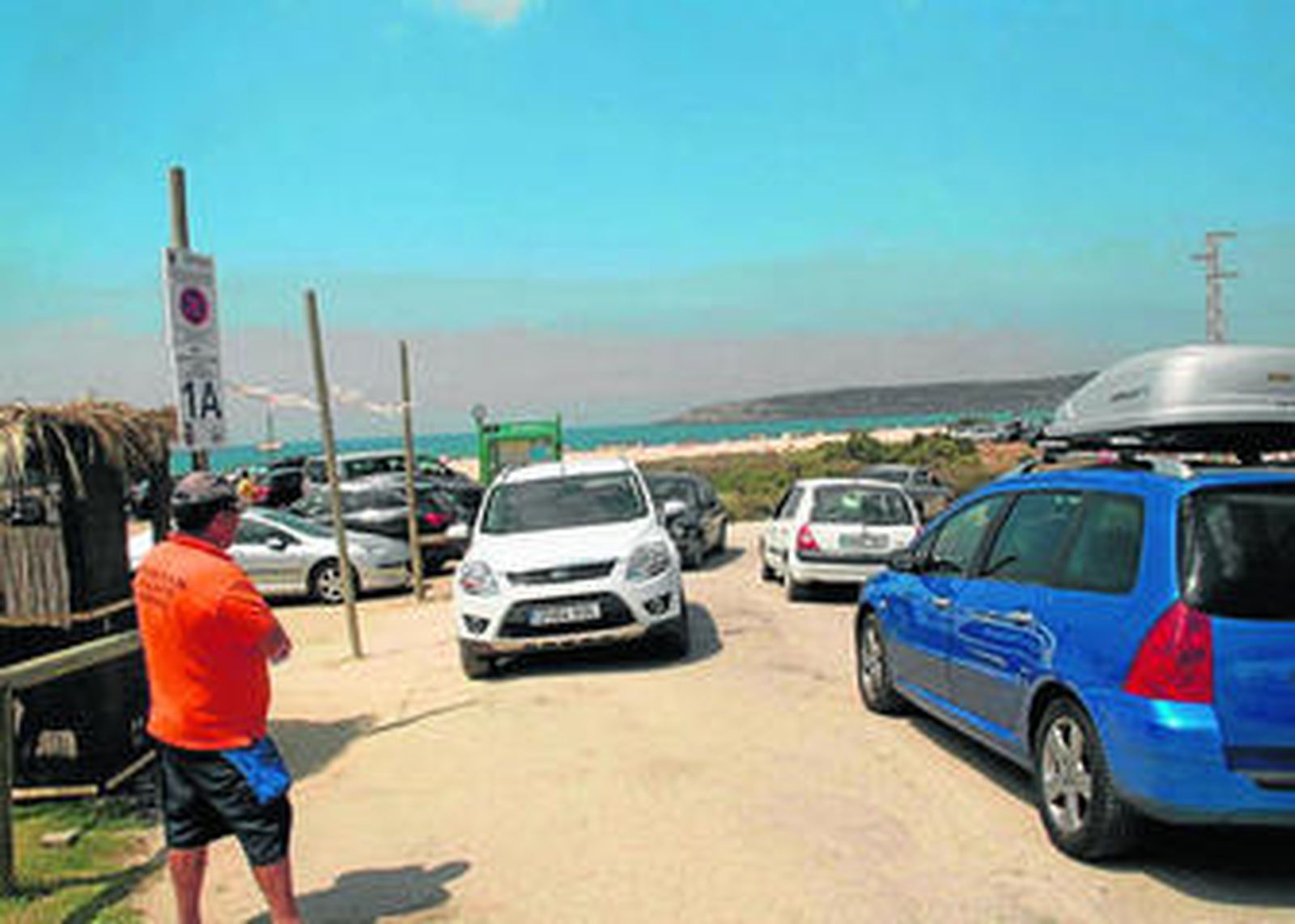 Vehículos entrando y saliendo en un aparcamiento junto a la playa de Los Lances.