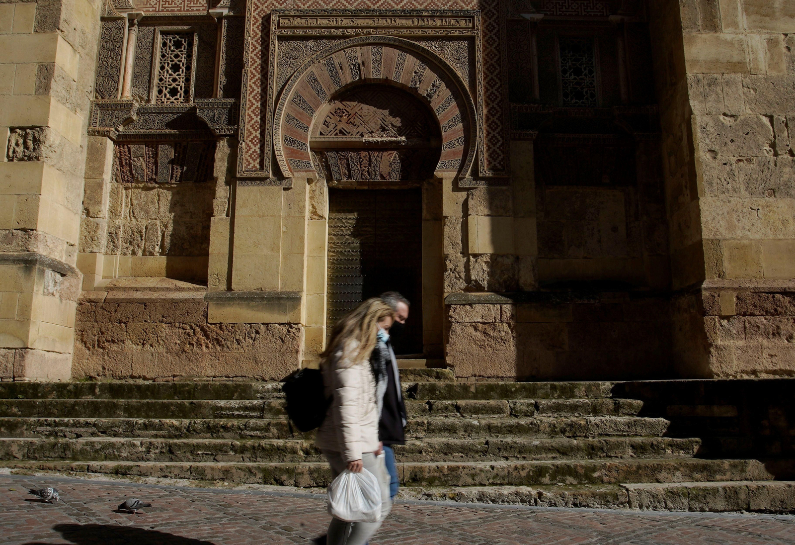 Dos personas caminan frente a la Mezquita-Catedral de Córdoba.