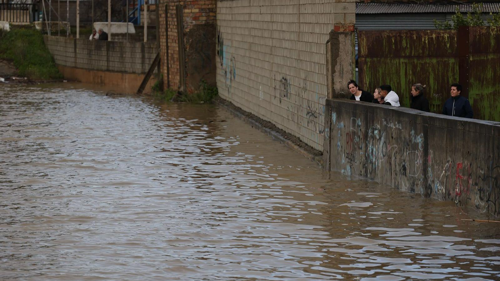 Vecinos de Lora miran expectantes el nivel del agua del arroyo Churre desde detrás de una tapia al final del muro de defensa, este viernes por la tarde.