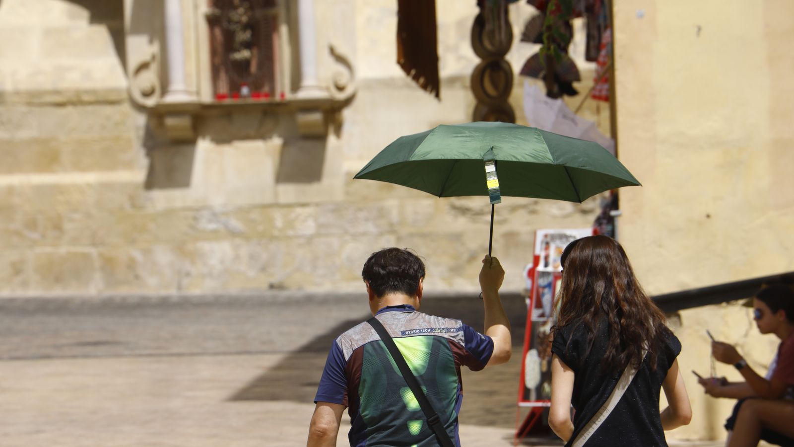 Una pareja de turistas se resguarda del calor bajo un paraguas.