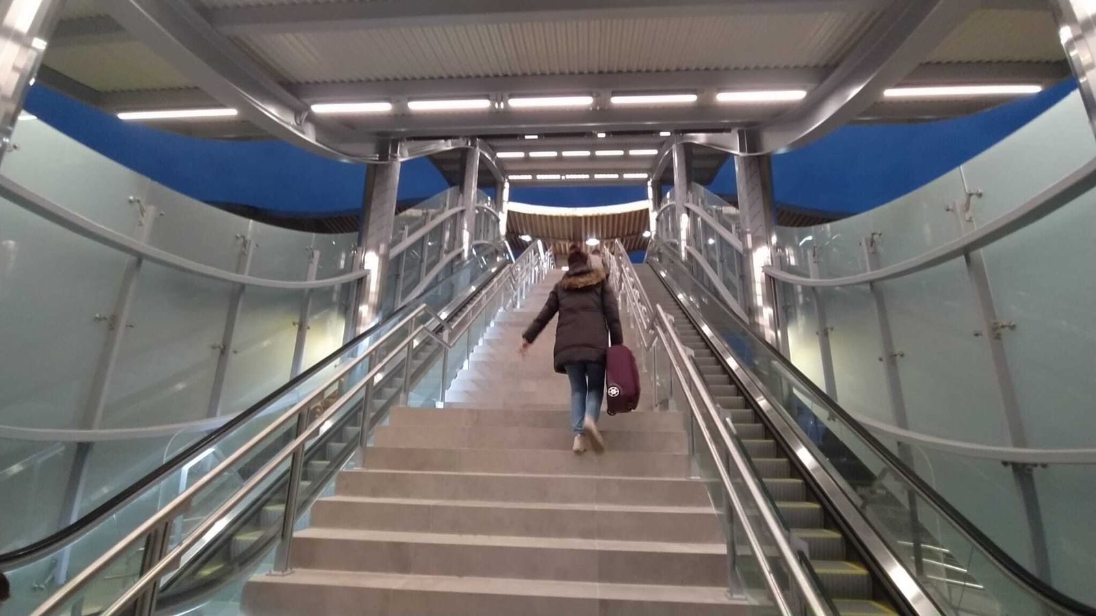 Usuarios de la estación, subiendo por la escalera con la maleta.